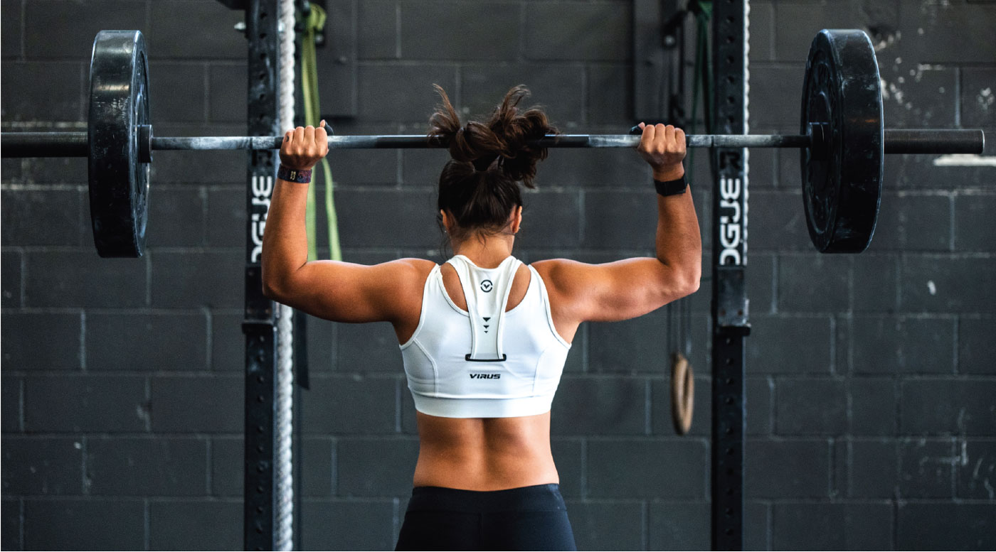 femme de dos à la salle de musculation qui soulève une barre chargée